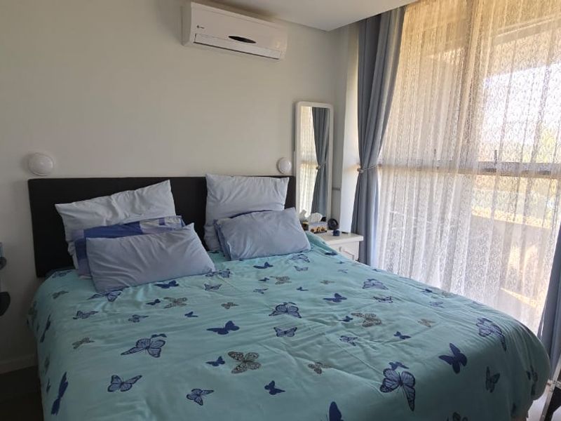 A functional bedroom featuring a wall-mounted split-system air conditioner and a large window with curtains, providing natural light and climate control.