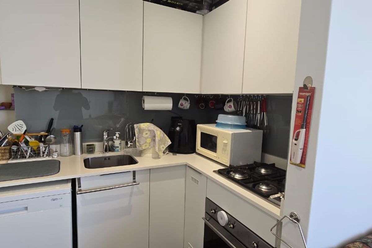 Compact modern kitchen featuring white cabinetry, integrated dishwasher, gas cooktop, built-in oven, and a sleek glass splashback.