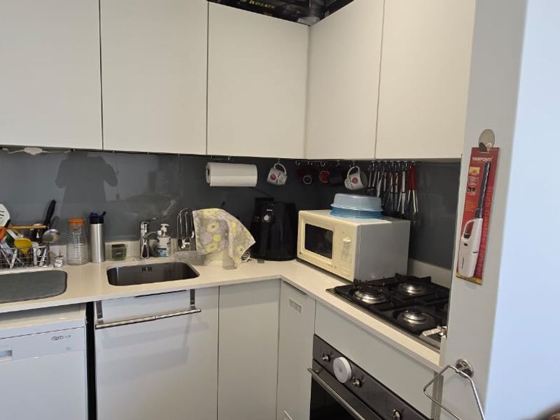 Compact modern kitchen featuring white cabinetry, integrated dishwasher, gas cooktop, built-in oven, and a sleek glass splashback.