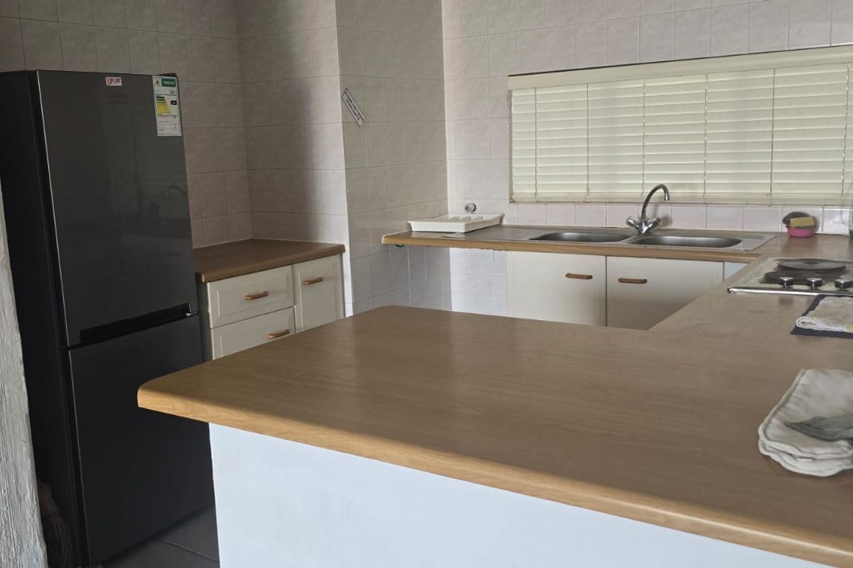 A functional kitchen featuring laminate countertops, built-in cabinetry, a double basin sink, and an integrated electric hob with tiled backsplash.