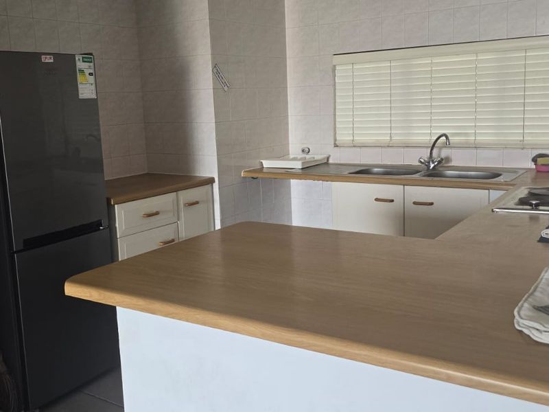 A functional kitchen featuring laminate countertops, built-in cabinetry, a double basin sink, and an integrated electric hob with tiled backsplash.