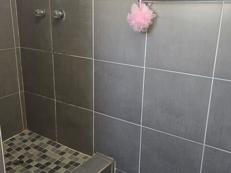 A functional shower enclosure featuring grey wall tiles, mosaic floor tiling, and standard shower mixer fixtures.