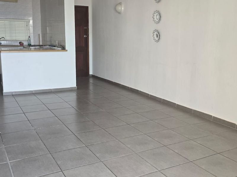 An open-plan living and kitchen area featuring neutral tiled flooring, a functional kitchen layout with cabinetry, and a breakfast counter.