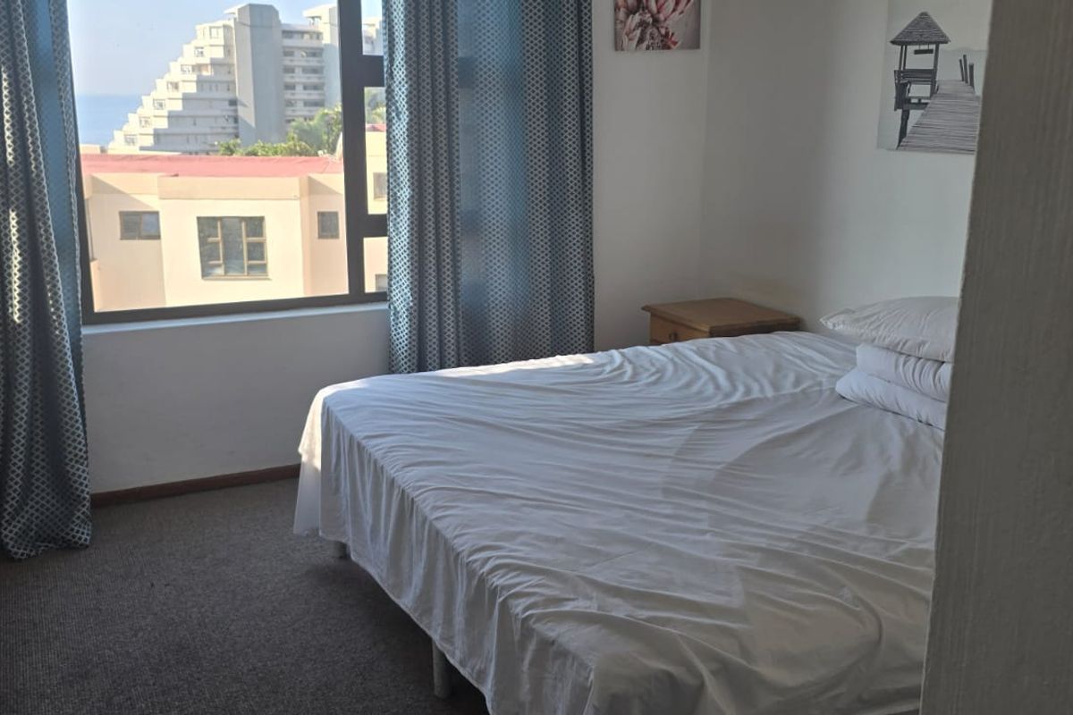 A bedroom featuring carpeted flooring, a built-in wardrobe, and a large window offering an urban view.