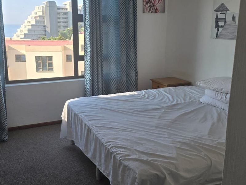 A bedroom featuring carpeted flooring, a built-in wardrobe, and a large window offering an urban view.