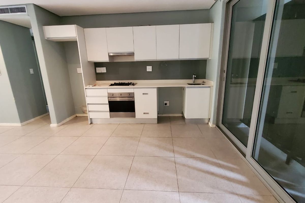 Modern open-plan kitchen featuring white cabinetry, built-in gas hob, oven, extractor fan, and tiled flooring, seamlessly connected to the living area via sliding doors.