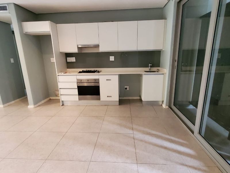 Modern open-plan kitchen featuring white cabinetry, built-in gas hob, oven, extractor fan, and tiled flooring, seamlessly connected to the living area via sliding doors.