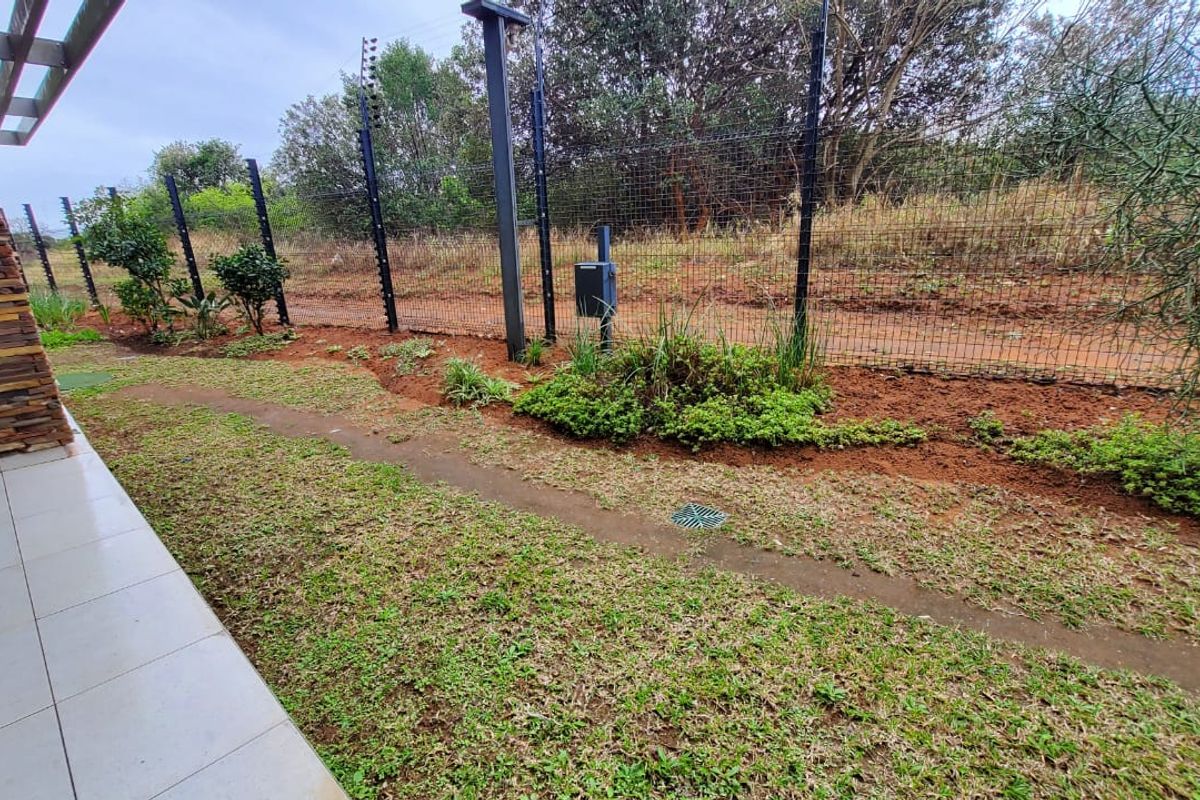 A rear exterior view of the apartment featuring a tiled patio, stone-clad wall, and a landscaped garden area enclosed by electric fencing.