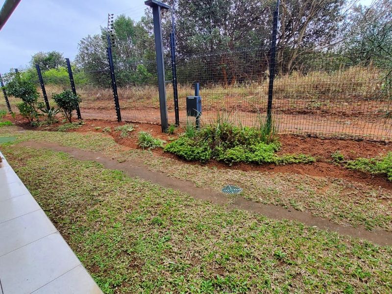 A rear exterior view of the apartment featuring a tiled patio, stone-clad wall, and a landscaped garden area enclosed by electric fencing.