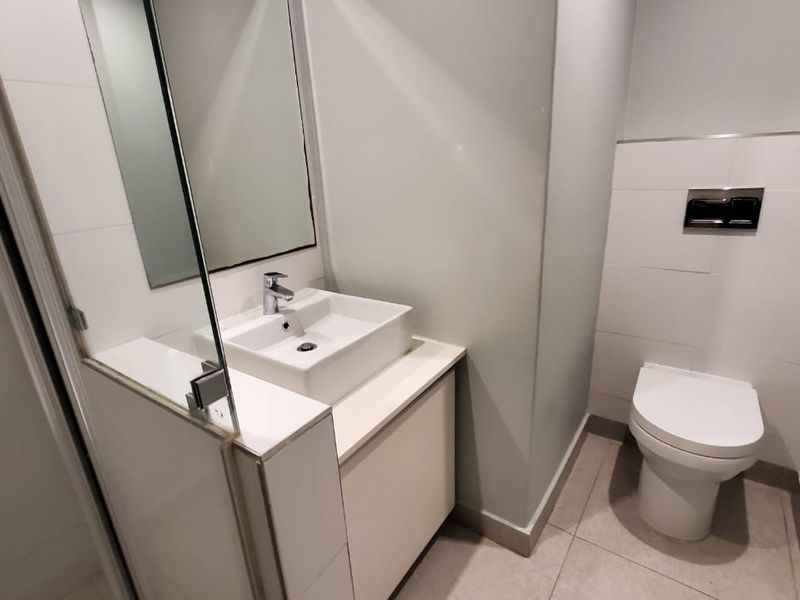Modern bathroom featuring a vessel sink with vanity cabinet, wall-mounted toilet with concealed cistern, and a glass-enclosed shower area.