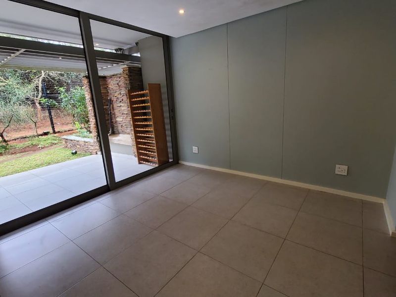 A bright, empty living area featuring large sliding glass doors that open onto a patio and garden, with modern tiled floors and neutral walls.