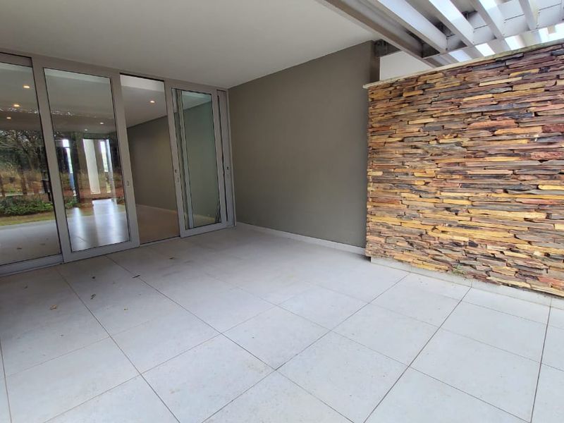 A covered patio area featuring large format floor tiles, a decorative stone feature wall, and sliding glass doors leading into the apartment interior.