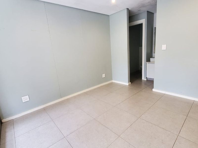An empty bedroom featuring neutral tiled flooring, recessed lighting, and a sliding glass door leading to an outdoor area.