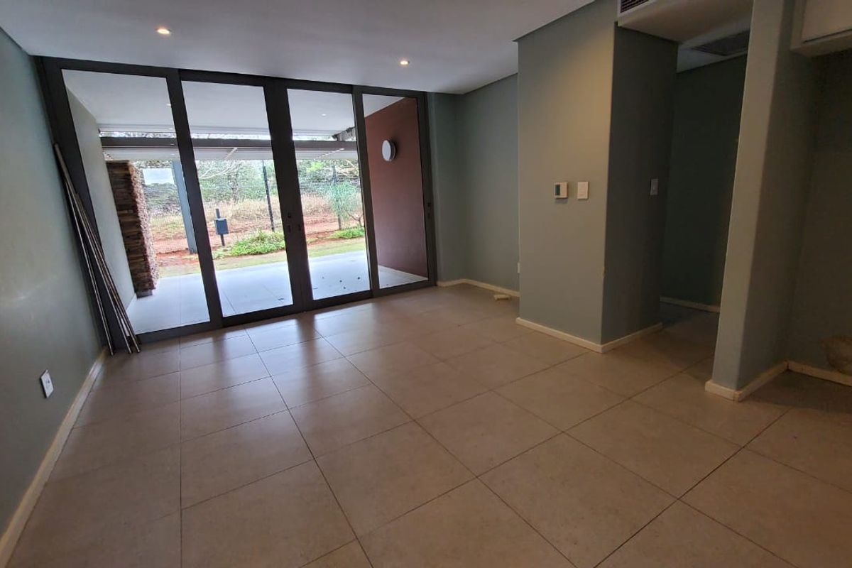 An empty living area featuring large sliding glass doors leading to an outdoor space, tiled flooring, and recessed lighting.