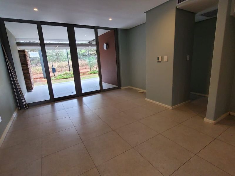 An empty living area featuring large sliding glass doors leading to an outdoor space, tiled flooring, and recessed lighting.