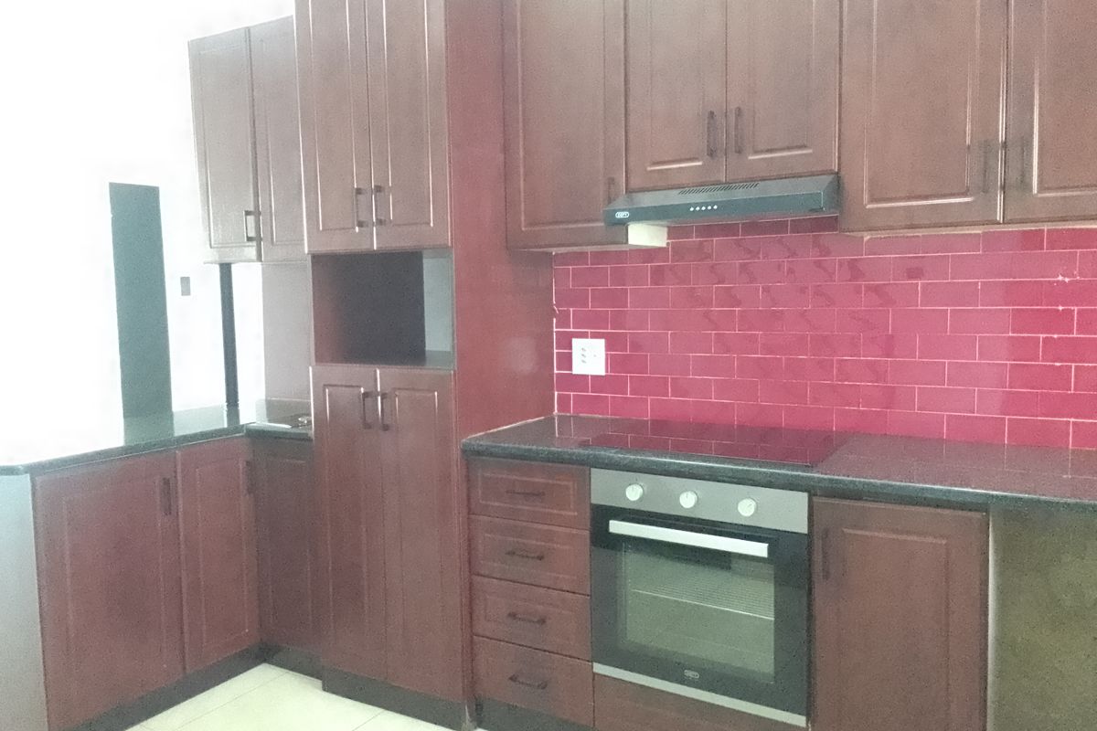 A functional kitchen featuring dark wood cabinetry, granite countertops, a built-in oven with hob, extractor fan, and a vibrant red tiled backsplash.