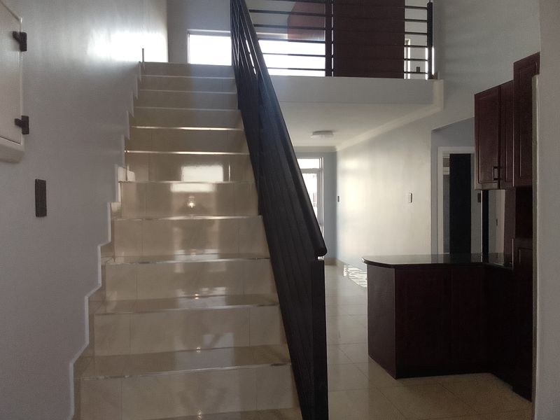 Open plan interior featuring a tiled staircase with metal balustrade, mezzanine level, and built-in kitchen cabinetry with granite countertops.