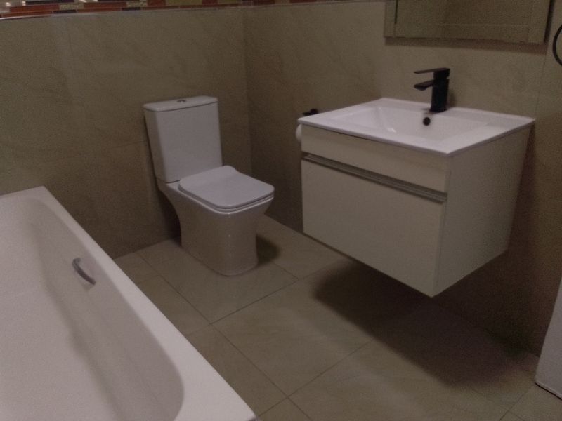 Modern bathroom featuring a wall-mounted vanity with a black mixer tap, a white toilet, and a bathtub with neutral tiled finishes.