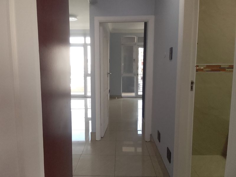 A bright, empty hallway with tiled flooring, connecting multiple rooms within the apartment.