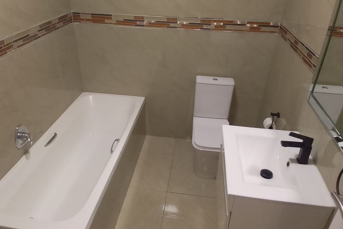 A clean, modern bathroom featuring a bathtub, toilet, and vanity basin with neutral wall and floor tiling.