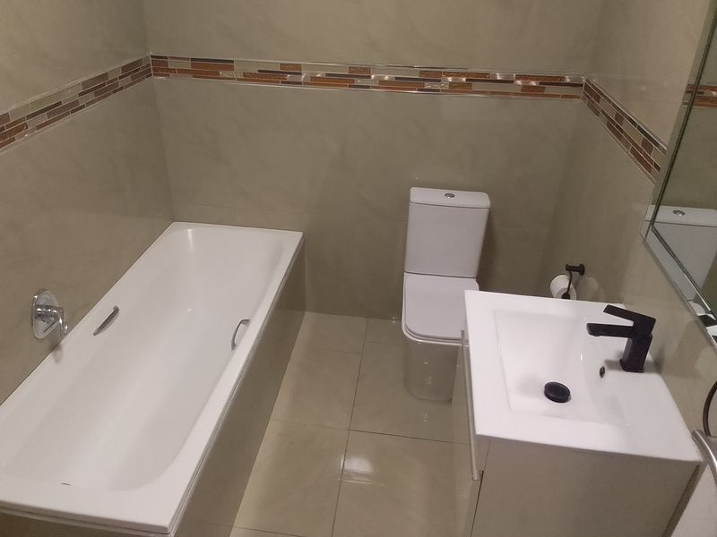 A clean, modern bathroom featuring a bathtub, toilet, and vanity basin with neutral wall and floor tiling.