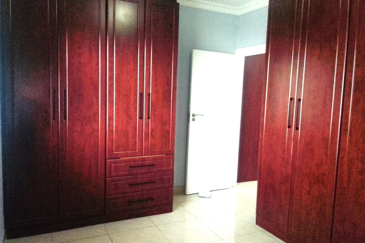 A bedroom featuring extensive dark wood built-in cupboards and neutral tiled flooring, offering ample storage space.