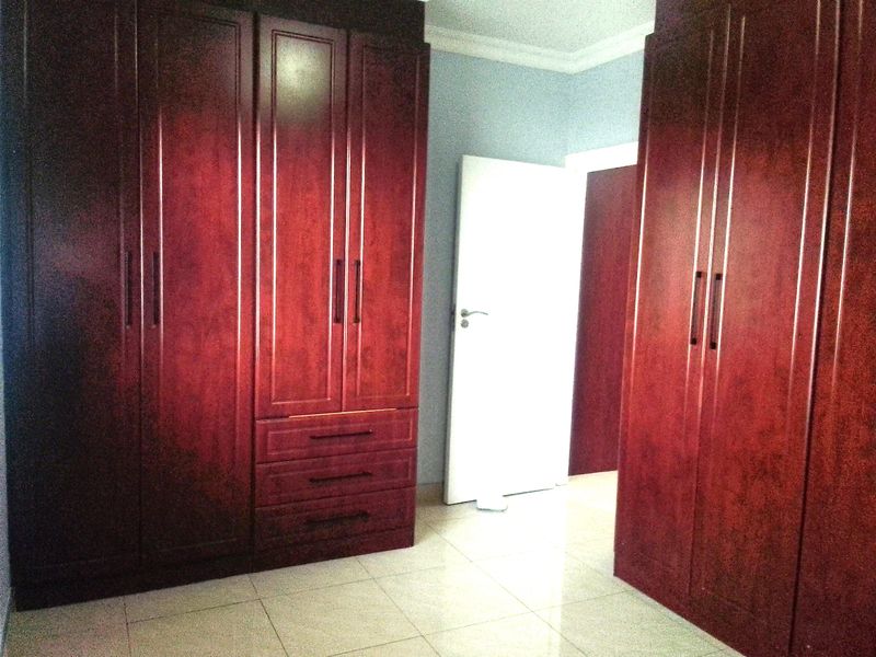 A bedroom featuring extensive dark wood built-in cupboards and neutral tiled flooring, offering ample storage space.