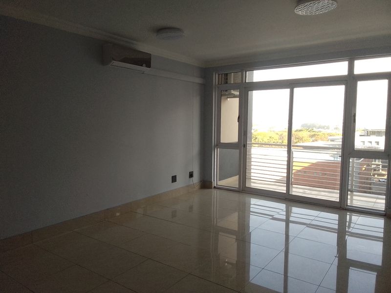 A bright, empty living room featuring polished tile floors, a wall-mounted air conditioning unit, and large sliding glass doors leading to a balcony.