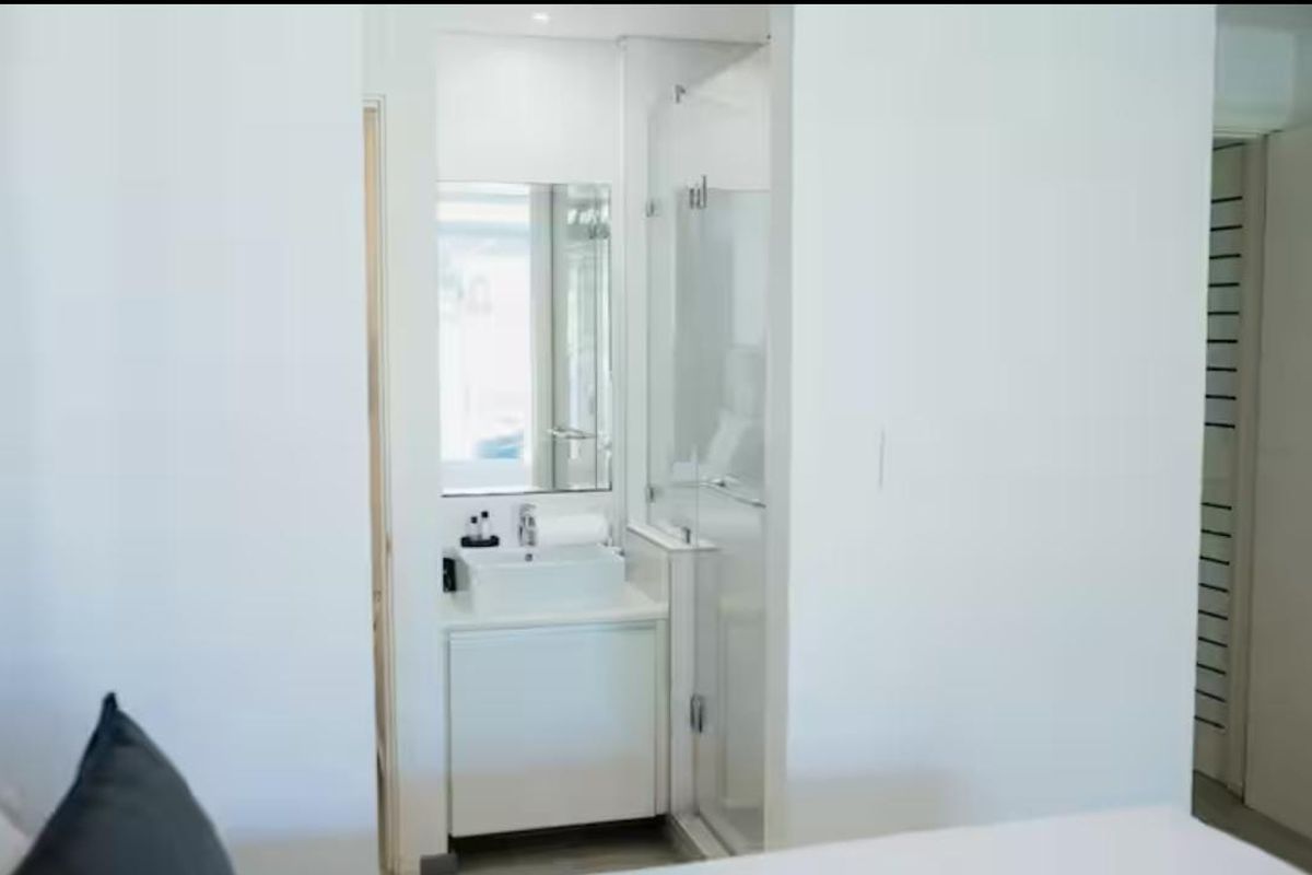A modern, compact bathroom featuring a white vanity with basin, wall-mounted mirror, and a glass-enclosed shower stall.