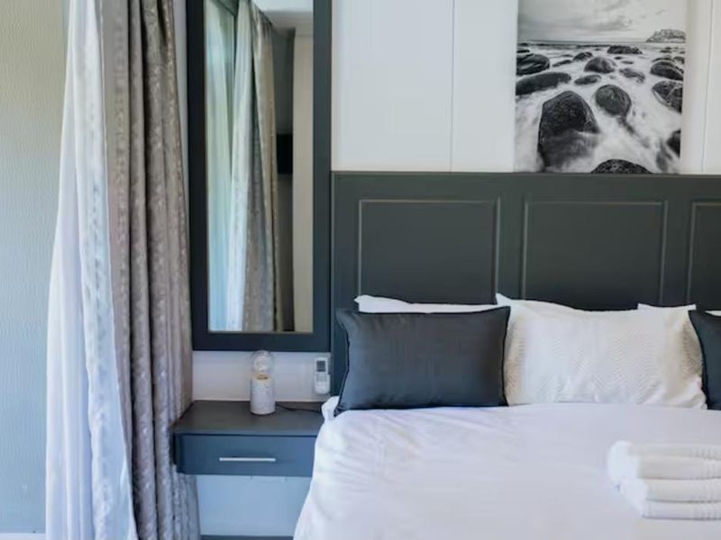 A well-appointed bedroom featuring a custom dark-toned built-in headboard, matching wall-mounted bedside table, and a vertical mirror.