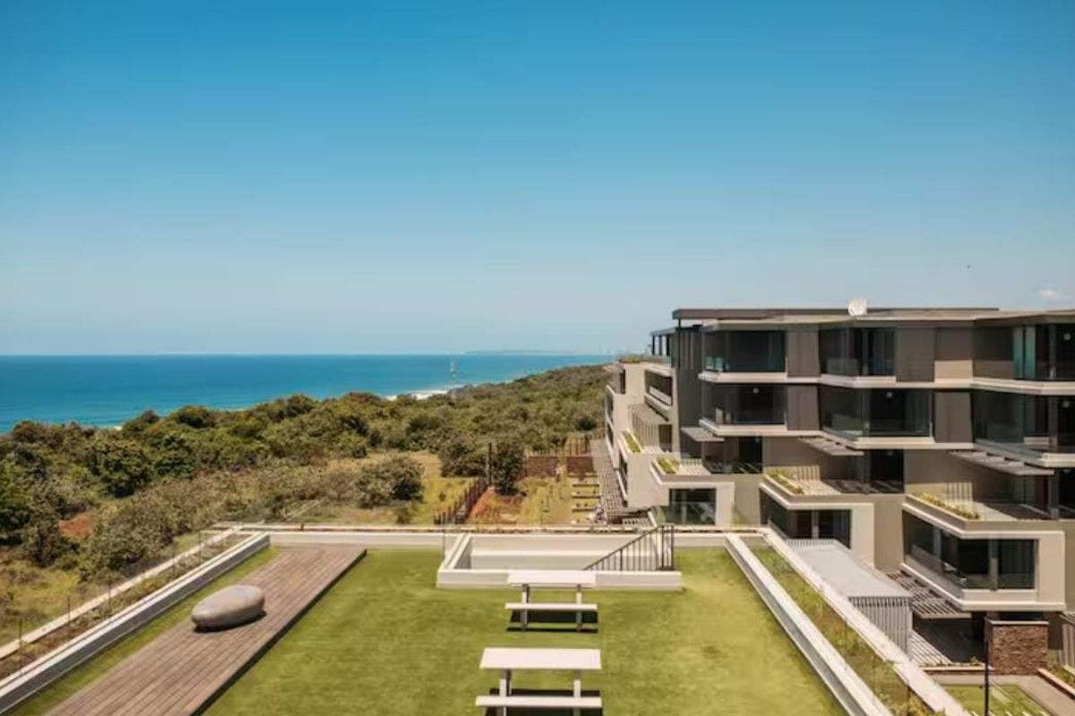 Aerial view of a modern apartment complex featuring a rooftop terrace with landscaped gardens, timber decking, and expansive ocean views.