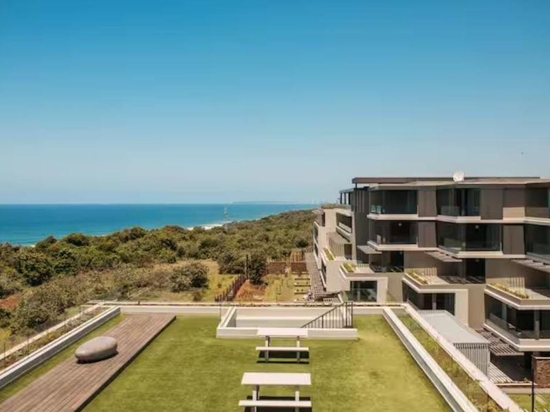 Aerial view of a modern apartment complex featuring a rooftop terrace with landscaped gardens, timber decking, and expansive ocean views.