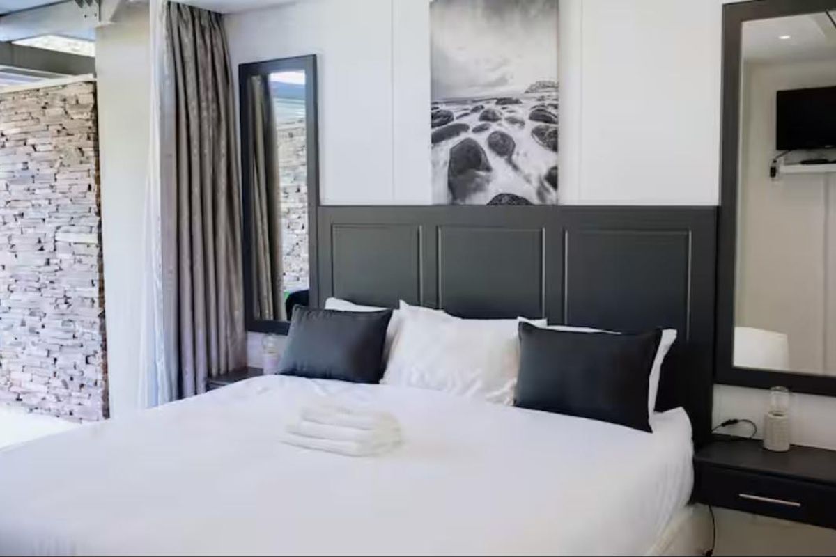 A well-appointed bedroom featuring a dark custom headboard, a textured stone feature wall, and integrated wall-mounted mirrors.