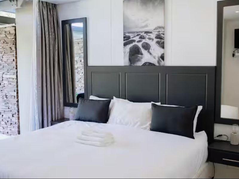 A well-appointed bedroom featuring a dark custom headboard, a textured stone feature wall, and integrated wall-mounted mirrors.