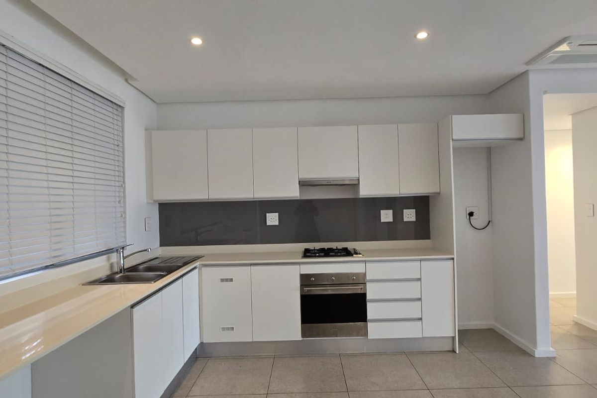 Modern kitchen featuring white cabinetry, stone countertops, integrated gas hob, electric oven, and sleek tiled flooring in a clean, minimalist design.