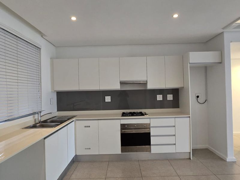 Modern kitchen featuring white cabinetry, stone countertops, integrated gas hob, electric oven, and sleek tiled flooring in a clean, minimalist design.