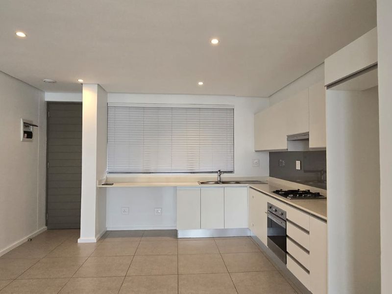 Modern open-plan kitchen featuring sleek white cabinetry, integrated appliances, tiled flooring, and recessed lighting in a clean, minimalist apartment setting.