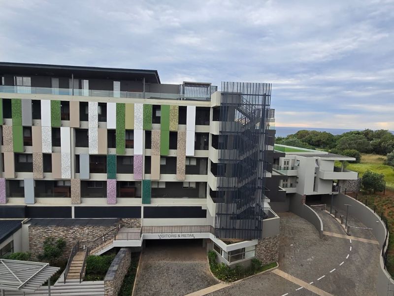 Modern multi-story apartment complex exterior featuring decorative facade cladding, external stairwell, paved visitor access driveway, and stone masonry retaining walls.