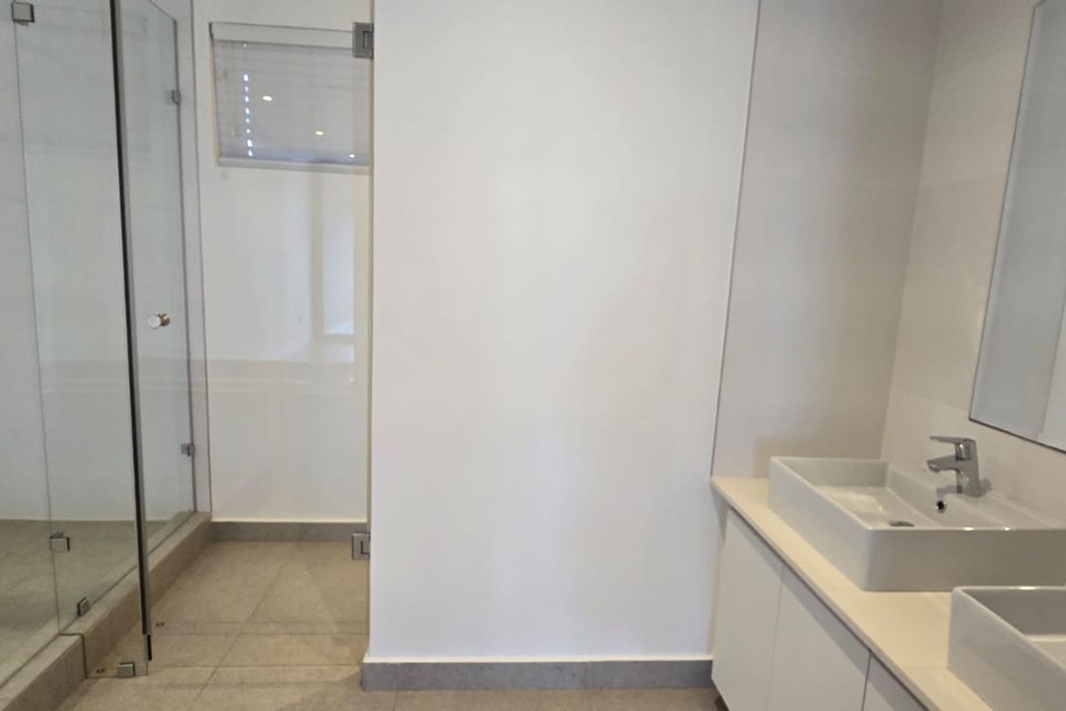 Modern bathroom featuring a double vanity with vessel sinks, a spacious glass-enclosed shower, and neutral tiled flooring.