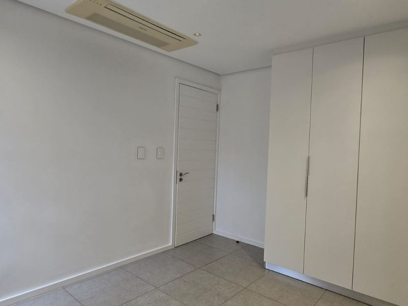 A clean, empty bedroom featuring neutral tiled flooring, a large built-in wardrobe, and a ceiling-mounted ducted air conditioning unit.