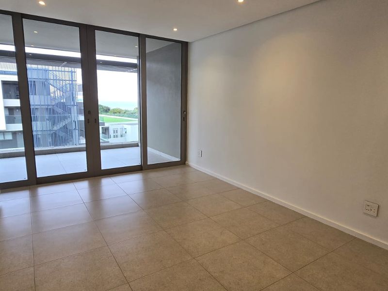 A bright, modern bedroom featuring neutral tiled flooring, ample built-in cupboard space, and large sliding glass doors leading to an outdoor balcony area.