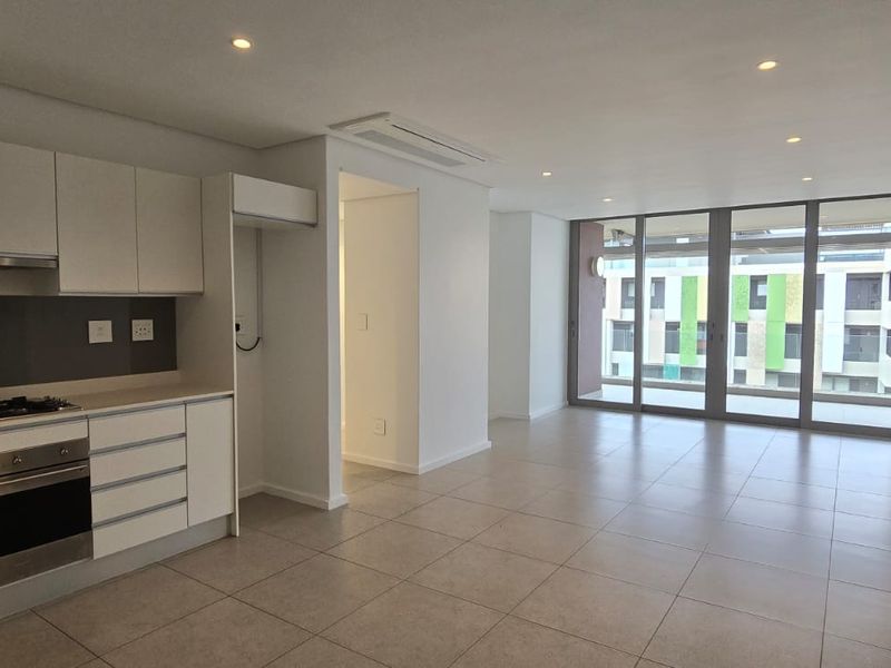 Modern open-plan kitchen and living area featuring sleek white cabinetry, integrated appliances, tiled floors, and large sliding doors leading to a balcony.