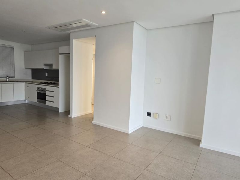 Spacious open-plan living area featuring a modern kitchen with built-in appliances, stone countertops, tiled flooring, and ducted air conditioning.