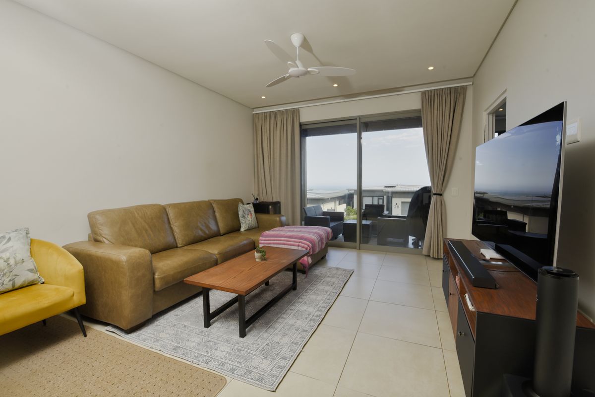 A well-maintained living room featuring tiled flooring, recessed lighting, a ceiling fan, and large sliding glass doors leading to an outdoor patio area.