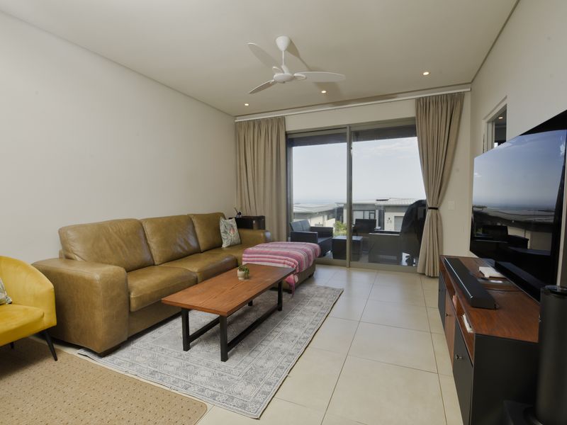 A well-maintained living room featuring tiled flooring, recessed lighting, a ceiling fan, and large sliding glass doors leading to an outdoor patio area.