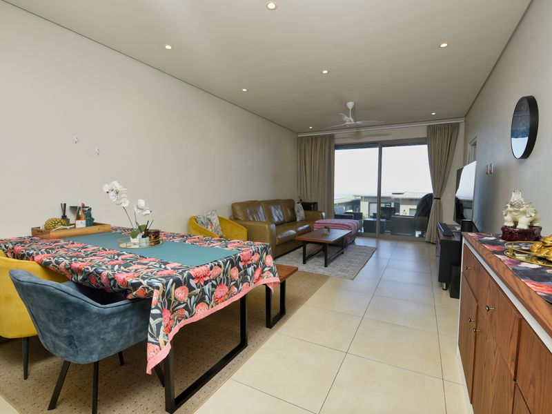 Spacious open-plan living and dining area featuring neutral tiled flooring, recessed lighting, and large sliding glass doors leading to an outdoor patio.