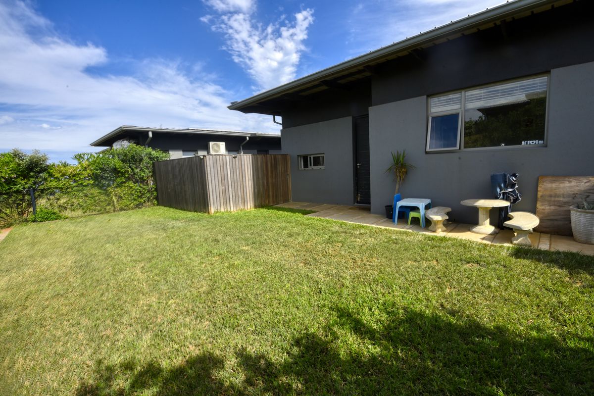 A private rear garden featuring a paved patio area, a timber privacy screen, and a well-maintained lawn adjacent to the townhouse exterior.