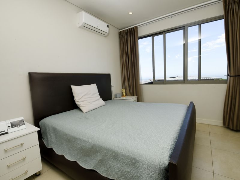 A well-maintained bedroom featuring tiled flooring, an integrated air conditioning unit, and large sliding windows offering natural light.