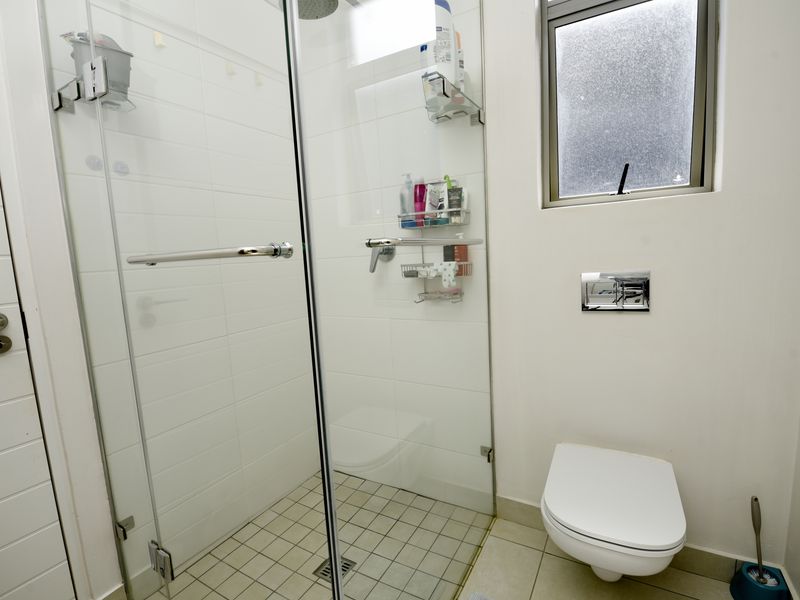 A modern bathroom featuring a glass-enclosed shower, wall-mounted toilet with chrome flush plate, and tiled flooring.