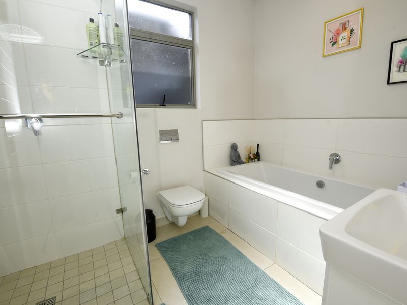 Modern bathroom featuring a glass-enclosed shower, a built-in bathtub, a wall-mounted toilet, and a clean tiled finish.